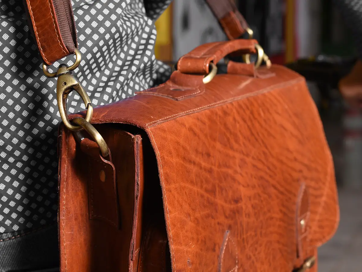 Gros plan sur une besace en cuir fauve, rabat, boucles et mousqueton en laiton